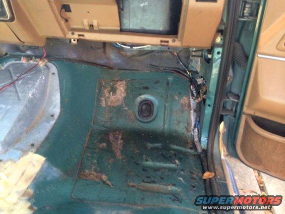 Green interior floor of a vehicle with exposed wiring and rust spots