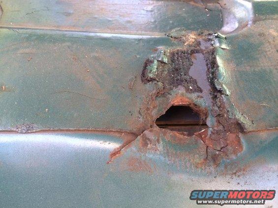 Green vehicle panel with large rust hole and peeling paint