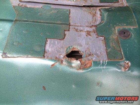 Green metal panel with rust holes and metal patches, showing signs of repair