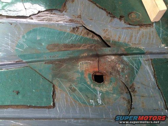 Rusted green metal floor pan with a square hole and cracks