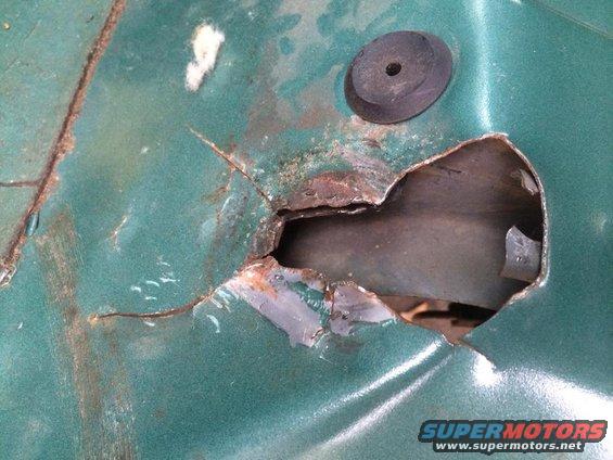 rusted hole in green metal panel with a black rubber grommet