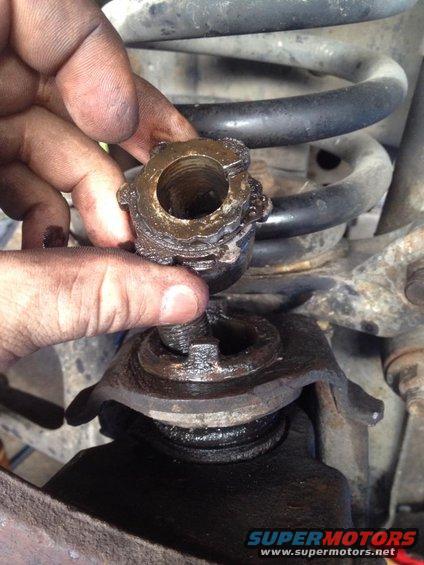 Hand holding a removed ball joint nut with suspension components and coil spring in background