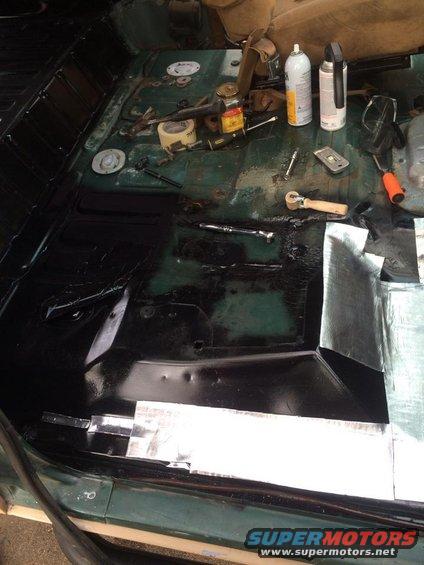Car floor being worked on, with sound deadening material and tools like a ratchet and spray cans