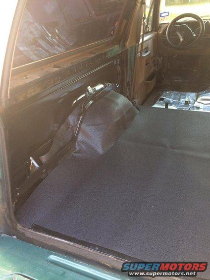 Interior of a vehicle with dark carpet on the floor and rear cargo area. The dashboard and steering wheel are visible