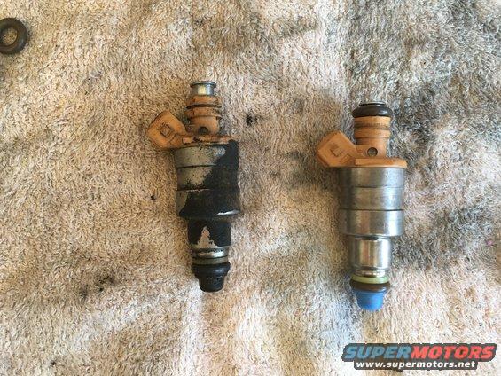 Two fuel injectors side-by-side on a towel. One is dirty and covered in black residue, the other is clean
