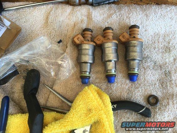 Three fuel injectors with blue caps and yellow O-rings on a towel, next to tools