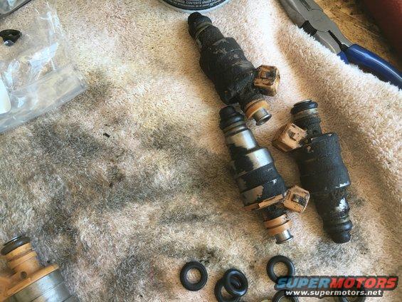 Four dirty fuel injectors and O-rings on a towel, with pliers in background