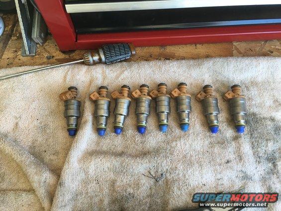 Eight fuel injectors laid out on a towel next to a red toolbox