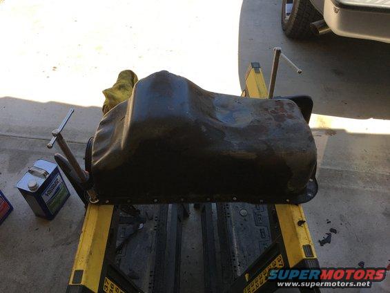 Oil pan resting on a yellow stand with a yellow rag and a can of fluid nearby