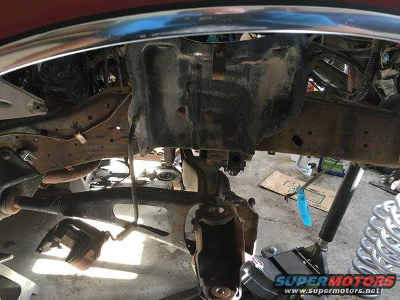 close-up of vehicle's front suspension and frame components, with parts removed and tools nearby