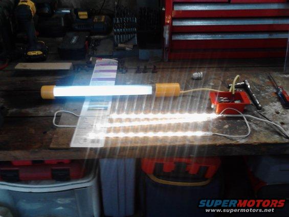Workbench with a fluorescent tube light and multiple LED strip lights powered on, tools and storage bins visible in the background