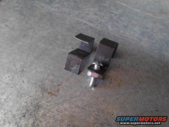 Two metal brackets, one with a bolt and washer attached, on a textured metal surface