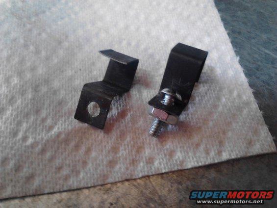 Two small black metal brackets, one with a bolt and nut attached, resting on a white paper towel