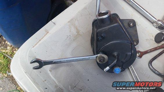 Power steering pump with a wrench attached, on a white surface