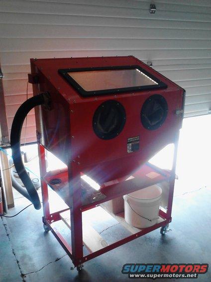 Red sandblaster cabinet on wheels with a clear viewing window and two glove ports