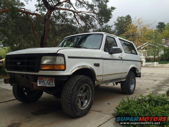 White 1995 Ford Bronco parked in a driveway with trees and a house in the background