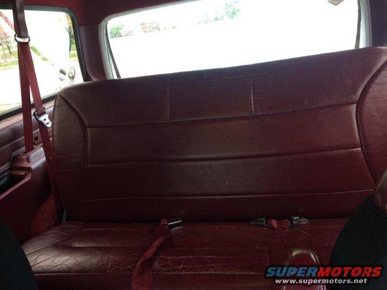 Maroon vinyl rear bench seat with red seatbelts and a visible seatbelt buckle