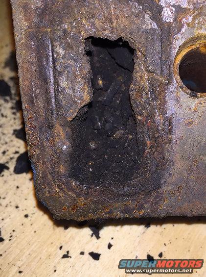 Heavily rusted metal part with a large hole showing internal debris