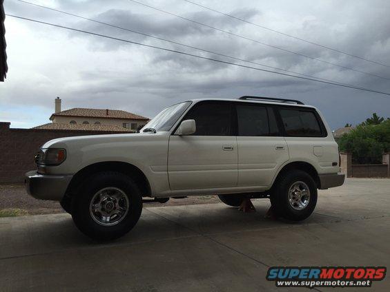 White Toyota Land Cruiser SUV parked on a driveway, side view, with a house and cloudy sky in the background