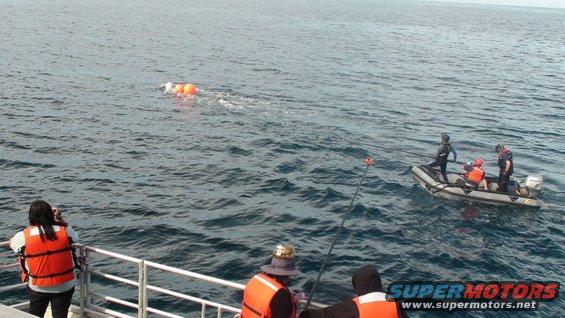Inflatable boat with people, fishing rod, and buoys in the water