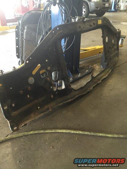 Black metal vehicle frame section with mounting holes and rust, on a workshop floor