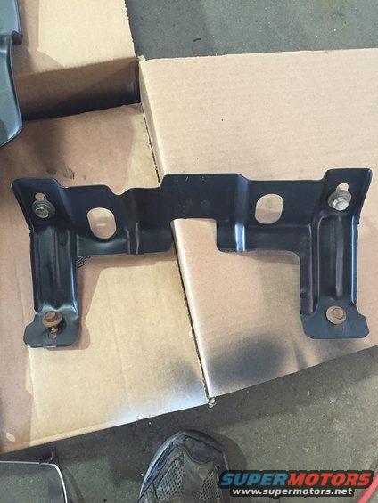 Black metal bracket with bolts, resting on cardboard