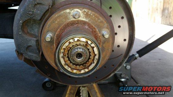 Close-up of a rusty front wheel hub assembly with a brake rotor and caliper
