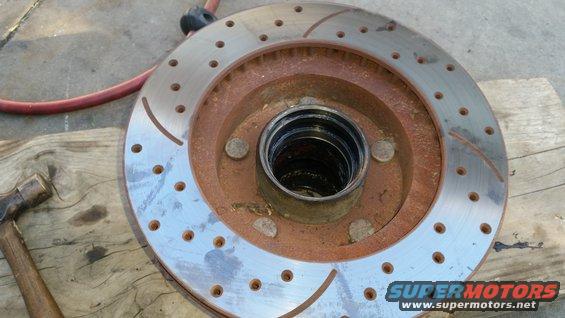 Slotted and drilled brake rotor with rust and a hammer on a wooden surface