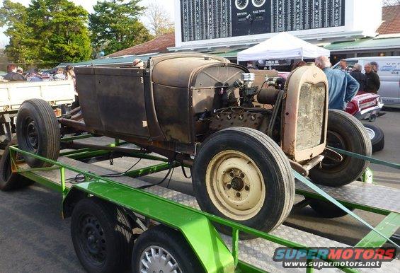Rusty hot rod body and engine on a green trailer, being towed