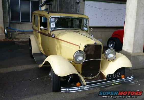 Yellow vintage sedan with a brown stripe, chrome bumper, and license plate 'TS 1932'