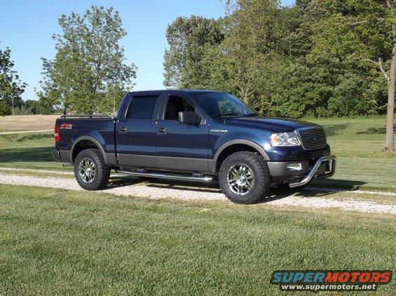 Blue Ford F-150 pickup truck with chrome accents and aftermarket wheels parked on a gravel driveway