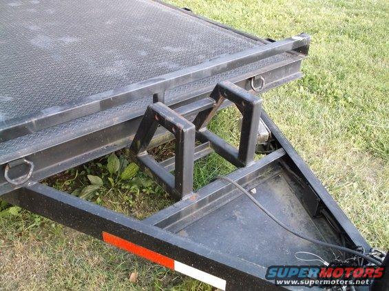 Close-up of a trailer's metal frame with diamond plate surface and tie-down rings. Shows a black metal structure with red and white reflective tape