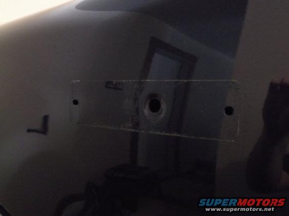 Close-up of a dark vehicle body panel showing two mounting holes and a central larger hole, possibly for a license plate bracket