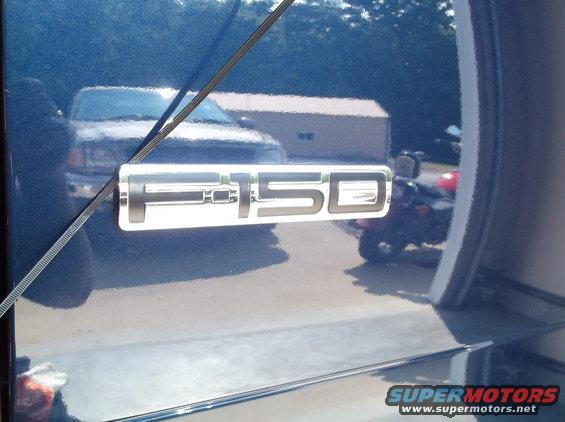 Blue Ford F-150 emblem on a blue truck door, with a reflection of another truck and a red ATV