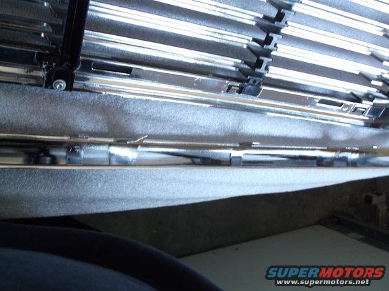 Chrome grille with horizontal bars and black clips, gray textured material below