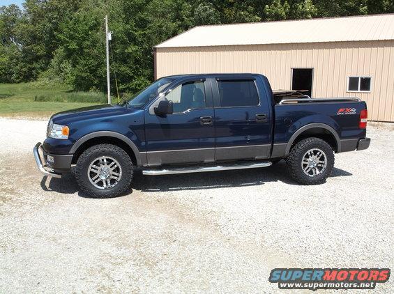 Dark blue crew cab pickup truck with aftermarket wheels and tires parked outside a building