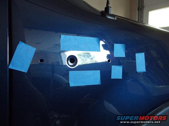 Blue vehicle fender with blue masking tape around a circular hole and two smaller holes