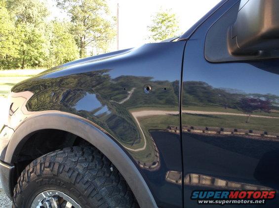 Dark blue pickup truck fender with two small holes and a larger hole next to them. Tire and wheel visible
