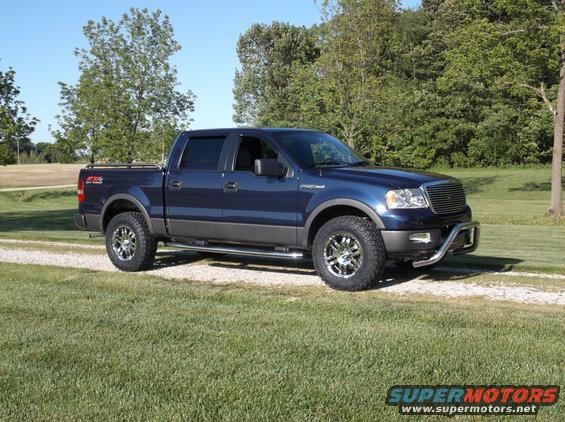 Blue 2005 Ford F-150 pickup truck with aftermarket wheels and bull bar parked on a gravel driveway