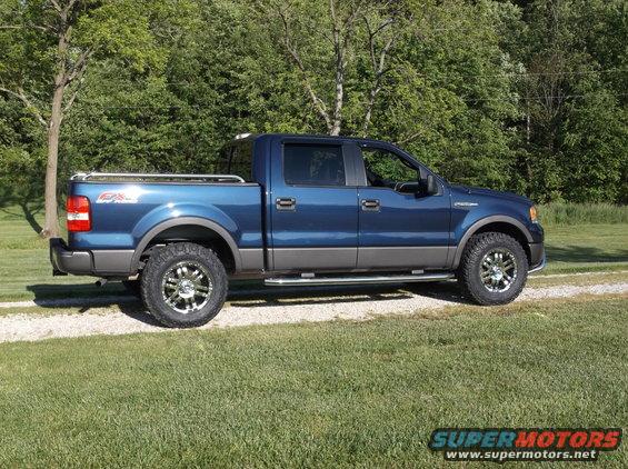 Blue pickup truck with gray trim and chrome wheels parked on a gravel driveway