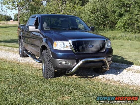 Dark blue Ford F-150 pickup truck with chrome grille guard parked on a gravel driveway