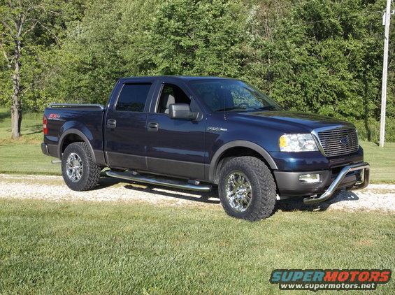 Dark blue Ford F-150 pickup truck with chrome wheels and a bull bar, parked on a gravel driveway