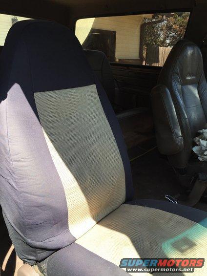 Interior view of a vehicle showing a fabric seat cover over the driver's seat and a leather passenger seat