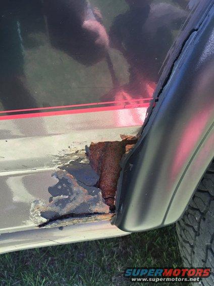 Close-up of severe rust damage on the lower body panel of a vehicle, near the rear wheel well