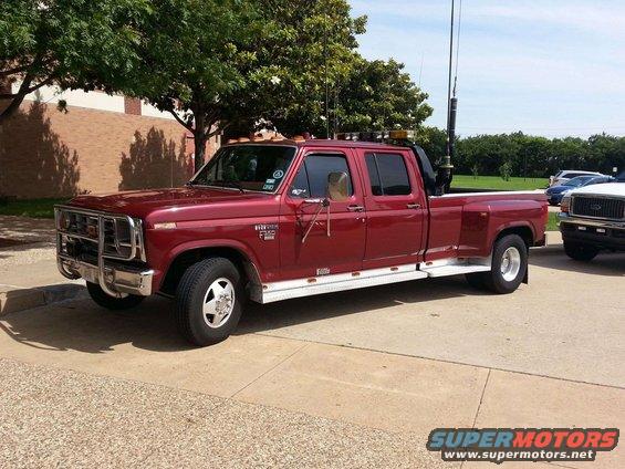 Maroon crew cab dually pickup truck with a push bumper and CB antennas. Another truck is parked to its right