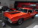 1971 Ford Ranchero - This orange muscle car, likely a 1970 model, is displayed indoors with other vehicles.