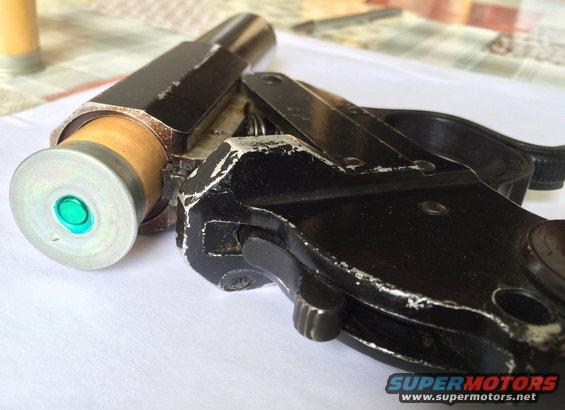 Close-up of a black flare gun loaded with a cartridge. The cartridge has a silver rim and a green primer