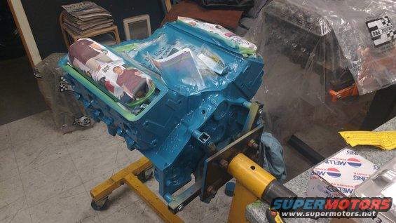 Blue engine block on yellow stand, covered with plastic and newspaper