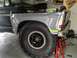 1979 Ford Bronco - The front fender and massive off-road tire of a 1979 Ford Bronco are visible, supported by red jack stands in a garage setting.