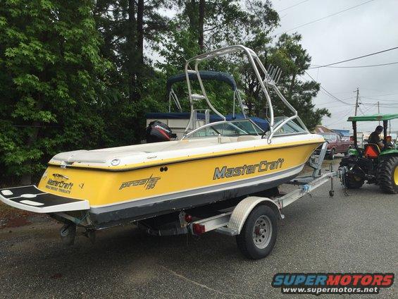 Yellow Mastercraft Prostar 190 boat on trailer, rear view. Tractor in background